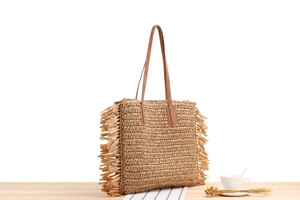 Detail of hand-woven straw shoulder bag with long side tassels and brown leather straps