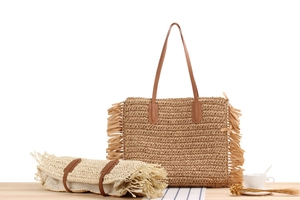 Detail view of woven paper rope tote bag set with tassels and brown leather handles