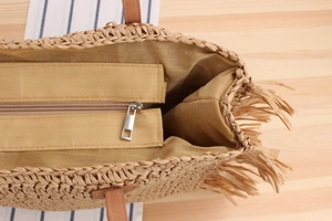 Detail of straw woven tote bag featuring long tassel trim and a secure metal zipper closure