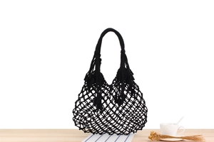 Close-up of black handmade macrame net beach bag on wooden table with white coffee cup