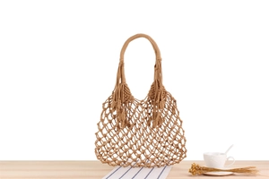 Detail view of khaki handmade woven mesh bag with boho fringe on a wooden table