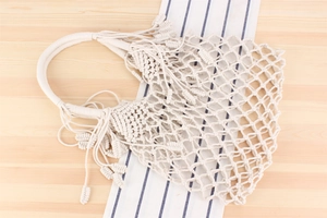 Detail of bohemian cream woven cotton net bag with fringe tassels on a wooden surface