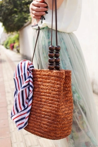 Dettaglio della borsa in paglia intrecciata con perle di legno e foulard di seta a righe