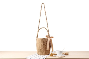 Detailed view of hand-woven straw bucket bag with ribbon bow on a wooden surface