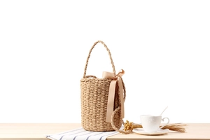Detail of hand-woven straw bucket bag with elegant champagne satin bow decoration
