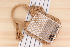 Detail of hand-woven mesh shoulder bag with long decorative tassels on wooden table
