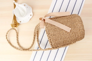 Detail of hand-woven straw bucket bag with champagne satin bow on a rustic wooden table