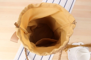 Detail view of woven straw bucket bag showing yellow fabric lining and drawstring closure