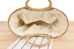 Detail view of woven straw tote bag with cream fabric lining and circular handles