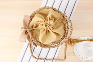 Close-up of woven straw bucket bag featuring a yellow canvas drawstring and silk bow