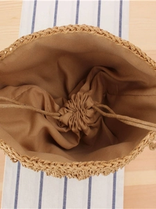 Handwoven straw bucket bag with secure drawstring lining on a wooden background