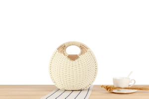 Detail of round straw bag with white woven texture and brown leather accents on table