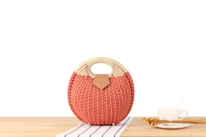 Detail of a bright orange woven shell bag with white handle and leather buckle on a table