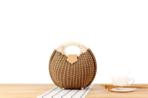 Detail of round woven shell bag featuring brown and white straw texture and leather clasp