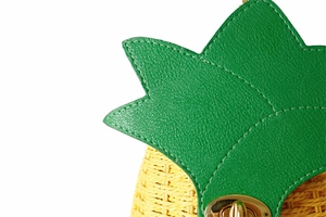 Détail du sac tressé ananas avec feuilles en cuir vert et fermoir rotatif en métal doré