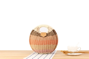 Detail of round woven straw handbag with colorful stripes and leather flap on wooden desk