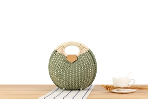 Detail of a round woven shell bag with green and beige patterns on a wooden table