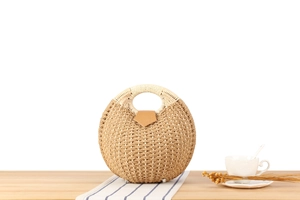 Detail view of a handcrafted shell-shaped woven straw handbag on a styled table