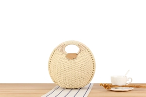 Close-up of a woven shell-shaped handbag with a brown leather clasp on a wooden desk