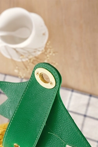 Détail du cuir litchi vert avec fermoir en métal doré et surpiqûres blanches contrastées