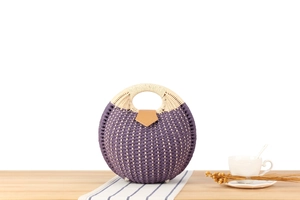 Detail of round woven handbag with purple grid pattern and brown leather snap closure