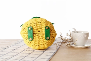 Détail du sac en paille ananas jaune avec brides en cuir vert et pieds en métal doré