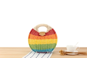 Detail view of a round rainbow woven handbag with circular handles on a wooden table