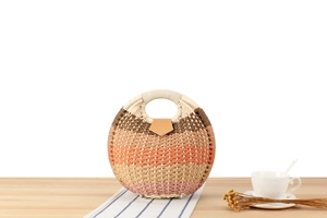 Detail of gradient woven straw handbag with round handle and leather buckle on wood table