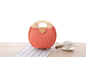 Detail of round handmade woven handbag featuring orange fiber textures and leather buckle