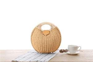 Detail view of a handcrafted round straw bag with a secure tan leather buckle and circular handle