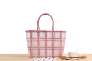 Detail view of a handmade pink and white checkered woven tote bag on a wooden table