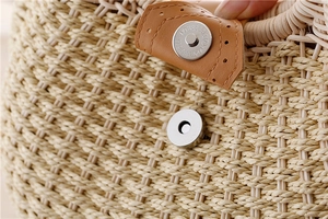 Close-up of metal magnetic buckle and brown leather trim on woven straw shell bag