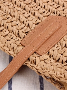 Straw shoulder bag with brown leather details and tassels on blue striped background