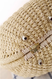 Close-up of woven straw handbag texture featuring silver cone studs and golden metal hinges