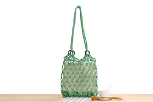 Green handmade woven net bag with cream drawstring liner on light wood surface