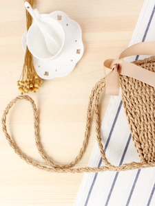 Minimalist straw woven bucket bag with silk ribbon detail on a rustic wooden table