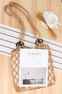 Detail of hollow woven cotton rope bag with wooden ring handles on a rustic table