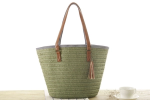 Detailed close-up of woven green beach tote with leather handles and decorative tassel