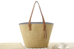 Detail of woven straw tote bag featuring brown leather handles and a fringe tassel charm