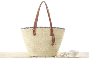 Detail of woven straw tote bag with brown leather handles and decorative tassel
