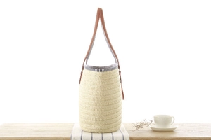 Detail of woven straw bucket bag featuring a brown leather handle and fringe tassel accent