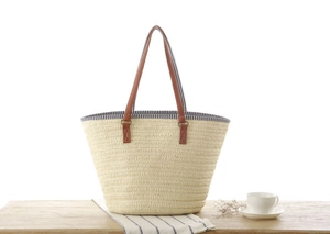 Detail of woven straw tote bag with brown leather handles and blue striped lining