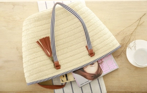 Detail of cream woven tote bag with blue striped straps and stylish leather tassel pendant