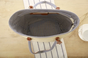Detail view of woven beach tote with blue striped lining and leather zipper pocket