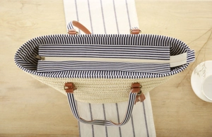 Detail of woven tote bag with blue striped lining, zip closure and leather handles