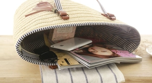 Detail of woven straw tote bag featuring blue striped lining and leather tassel charm