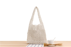 Detail of hand-woven cream mesh bag with inner lining on a wooden table with coffee cup
