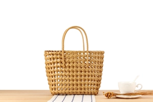Close-up of light brown woven PVC basket bag with sturdy handles on a wooden table
