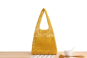 Detail of yellow hand-woven crochet mesh tote bag showing inner lining on wooden table