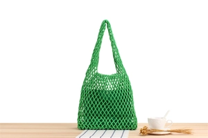 Handmade woven mesh tote bag in grass green with matching inner pouch on a wooden table